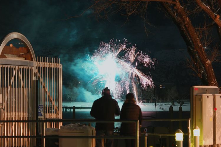 Rear view of people watching firework display at night