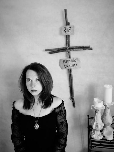Portrait of sad woman standing with cross and text hanging on wall