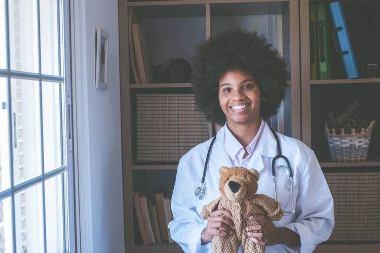 Portrait of smiling doctor holding stuffed toy at clinic