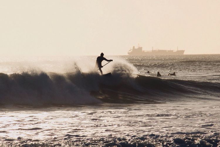 Silhouette man surfing on sea against clear sky
