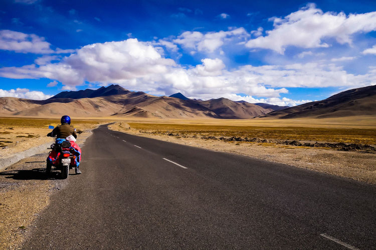 Rear view of mid adult man riding motorcycle on road against sky
