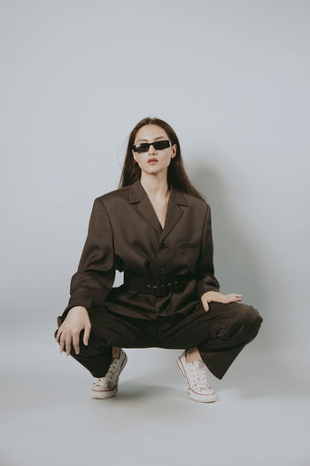 Young woman wearing sunglasses sitting against white background
