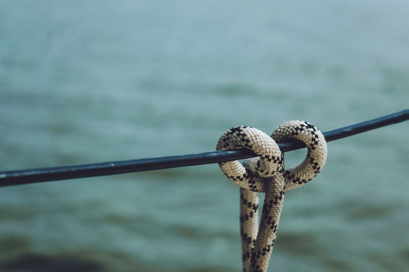 Close-up of rope tied to metal cable against sea