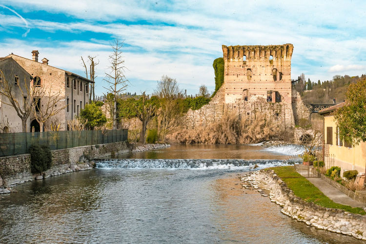 Old building by river against cloudy sky