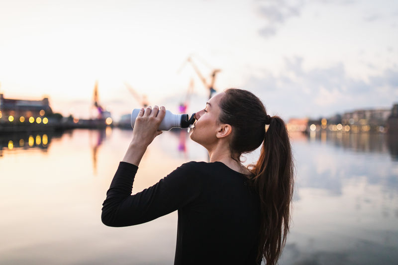 Side view of woman drinking water against sky