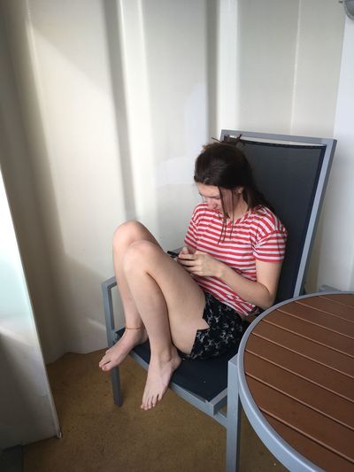 Young woman using phone while sitting on chair at home