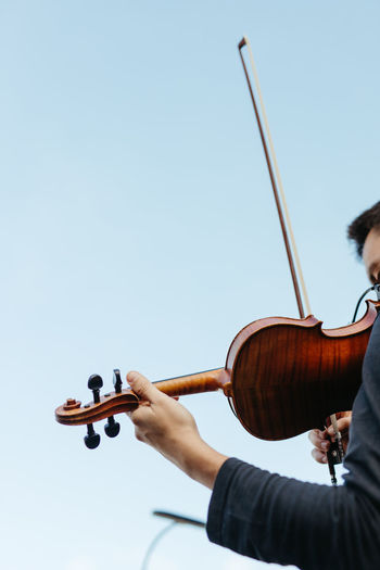 Cropped hand holding violin against clear sky