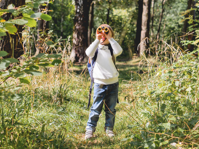 Full length of boy looking through binoculars in forest