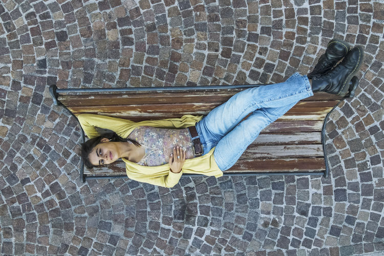 Italy, apulia, erchie, aerial view of young woman lying on bench
