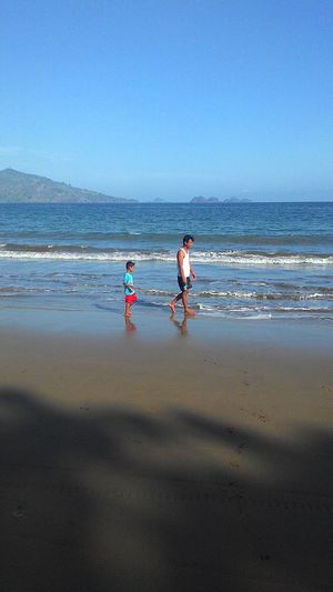 Father and son walking at beach against clear sky