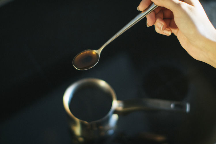 Cropped image of hand holding spoon over container