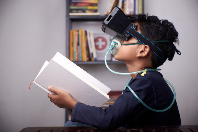 Side view of boy wearing virtual reality simulator while holding book