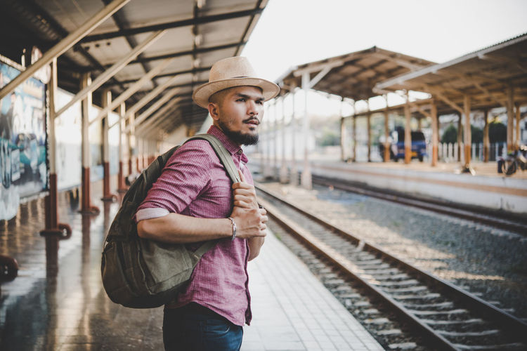 Side view of man with backpack standing at railroad station