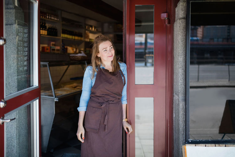 Female owner wearing apron standing on entrance of store