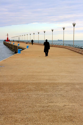 Two people walking on the pier, towards the sea, at the sunset