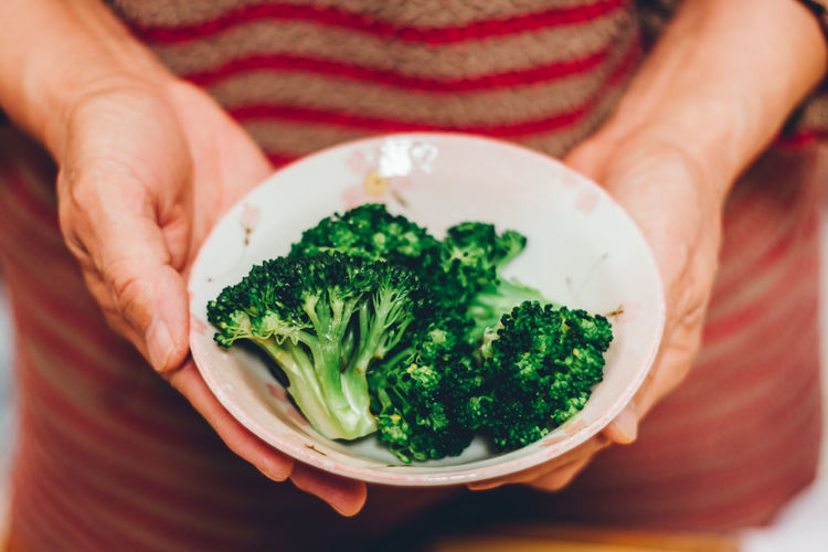 The midsection of senior woman holding steamed broccoli in the bowl. / housewife / cooking at home