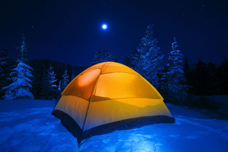Illuminated tent on snow covered land against sky at night