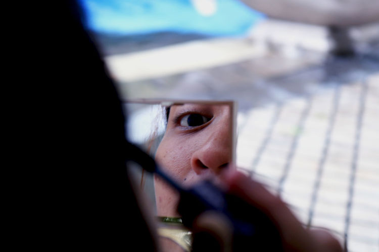 Close-up of woman applying make-up reflecting on hand mirror