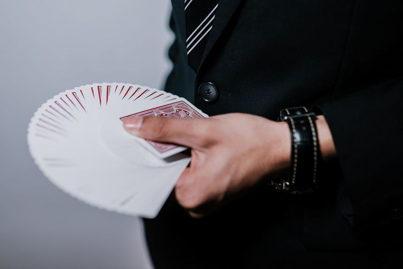 Midsection of man holding playing cards against gray background