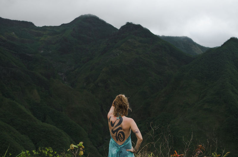 Rear view of woman with tattoo on back standing against mountains 