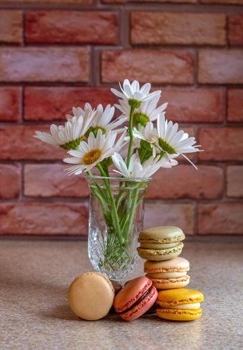Delicious macaron cookies are stacked next to a pretty vase with daisies