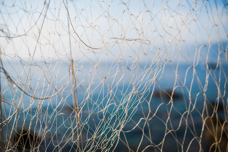 Close-up of fishing net with sea in background