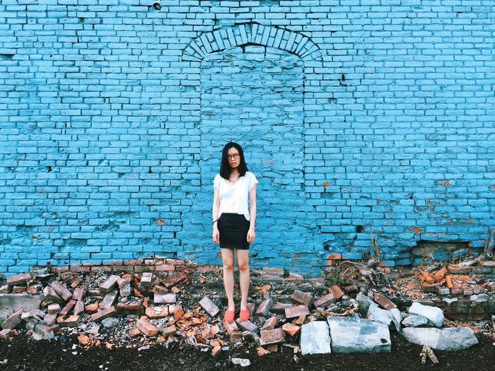 Full length of woman standing amidst bricks against blue wall