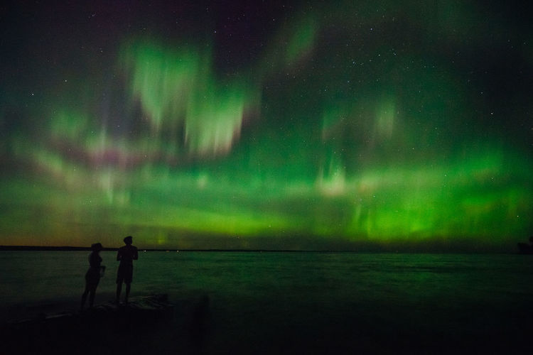 Silhouette couple standing at beach against aurora borealis at night