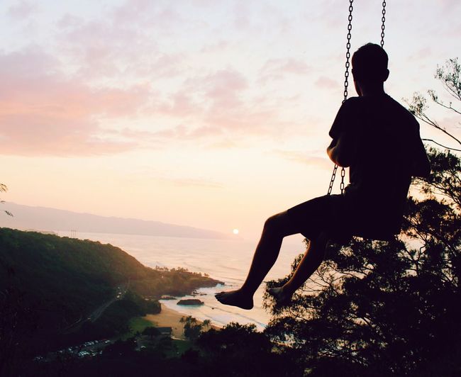 Silhouette man sitting on swing at sunset