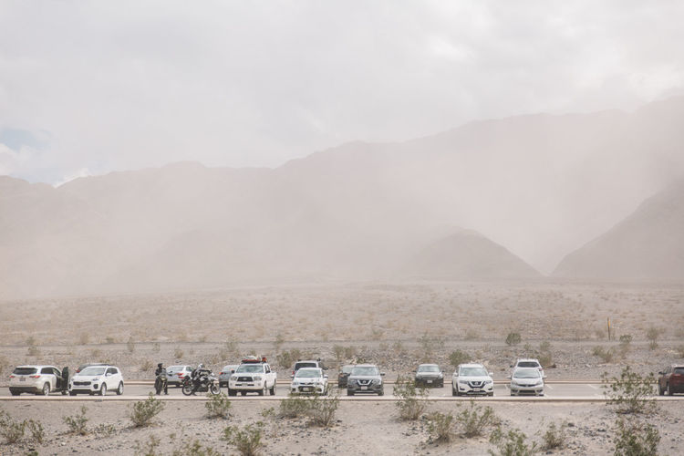 Vehicles parked at parking lot against mountains at death valley during sandstorm