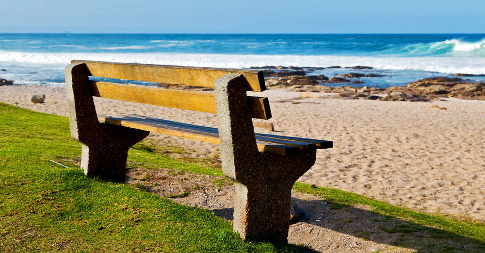Bench on beach by sea against sky
