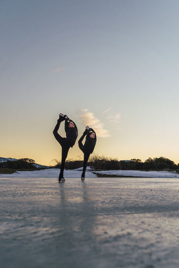 Two female figure skaters practicing together on frozen lake at dusk