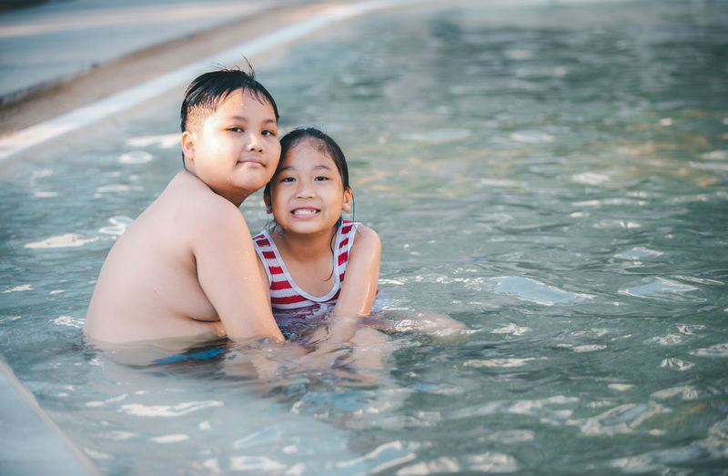 Happy brother and sisiter are playing water at swimming pool, recreation and relax on summer