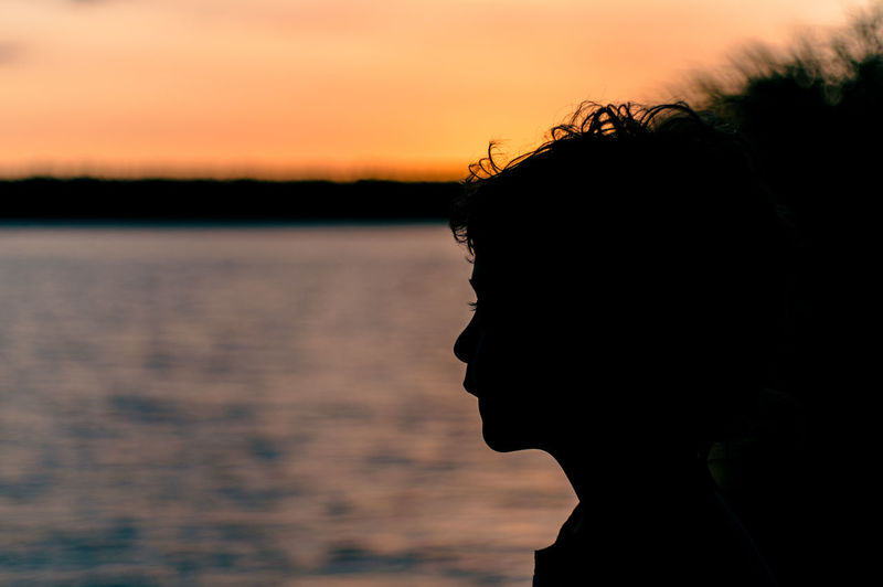 Close-up portrait of silhouette boy against lake during sunset