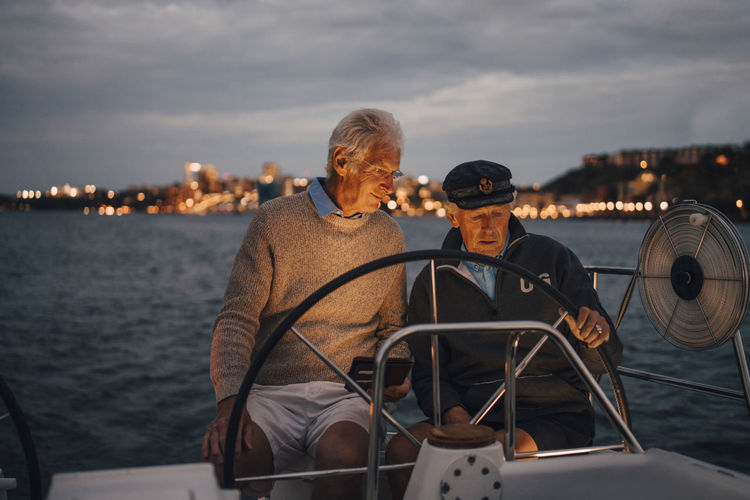 Senior man guiding male friend while sailing boat during sunset