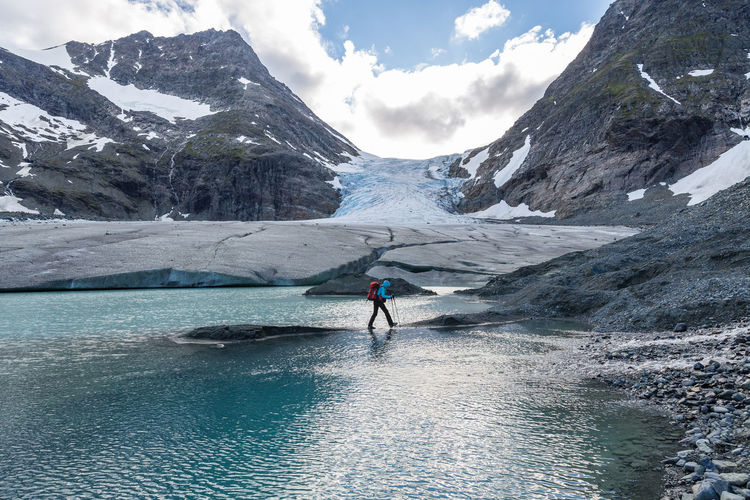 Side view of person hiking at glacier lake against mountains