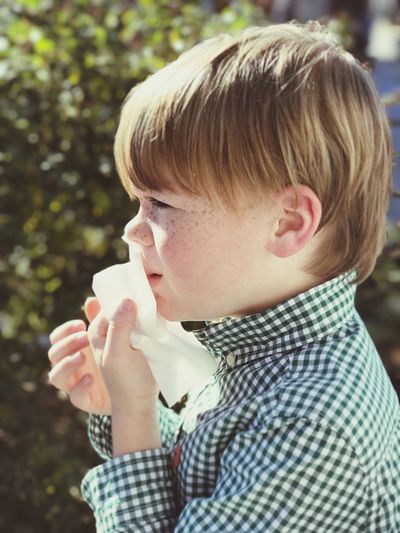 Side view of boy wiping mouth with facial tissue during sunny day