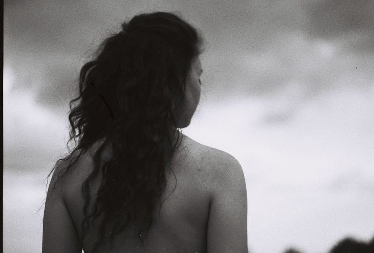 Rear view of shirtless woman against sky