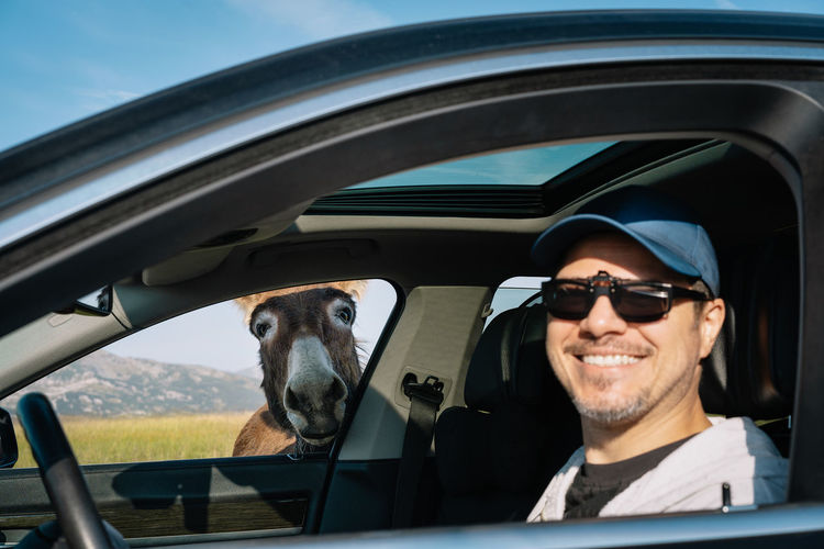 Portrait of smiling man in car with donkey outside car