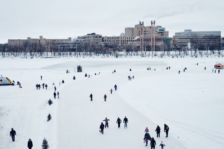 People skating on snow covered field against sky