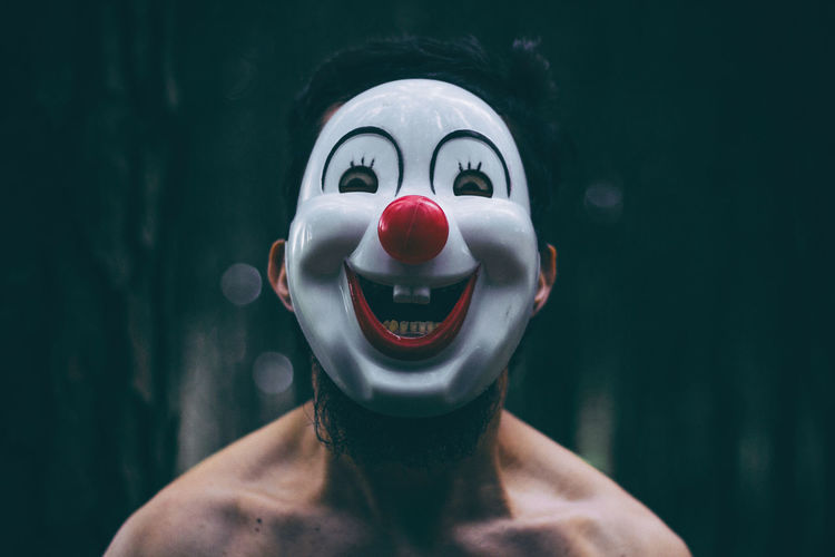 Portrait of shirtless mid adult man wearing clown mask while standing outdoors
