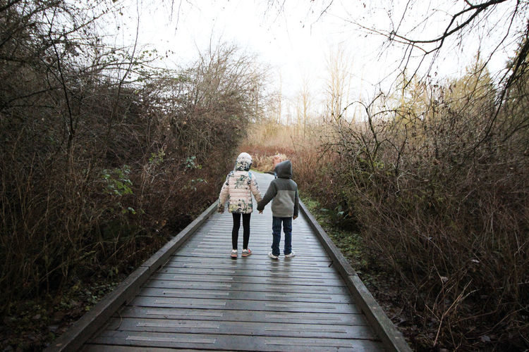 Rear view of siblings standing on footpath amidst trees
