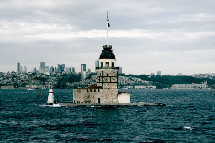 View of lighthouse in sea against buildings in city