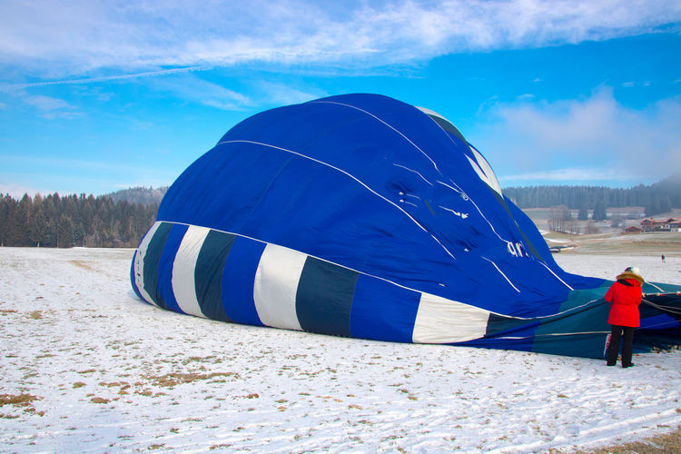 Rear view of man deflating hot air balloon after flight against cloudy sky