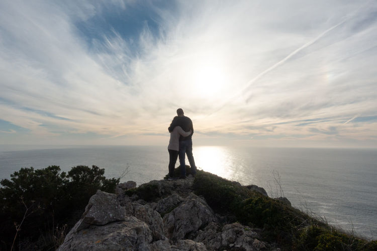 Romantic couple silhouette holding eachother at a cliff in cabo espichel cape in portugal