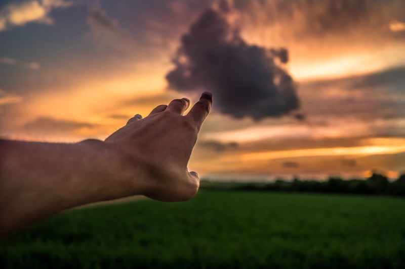 Optical illusion of man touching cloud during sunset