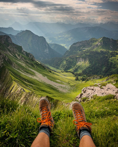 Low section of person wearing shoes sitting by cliff against sky