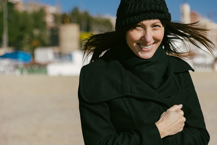 Smiling woman in hat and coat on the beach on a sunny winter day