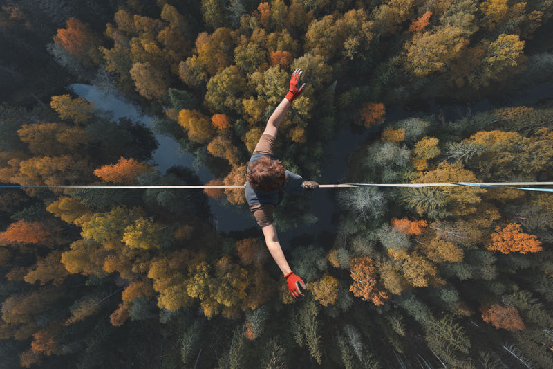 A breathtaking view of a tightrope walker walking along a line high above a beautiful forest.