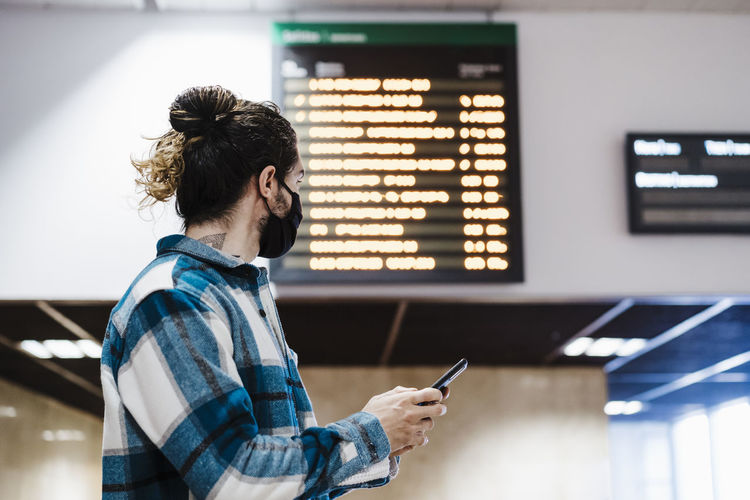 Young man wearing face mask using mobile phone while waiting at subway station